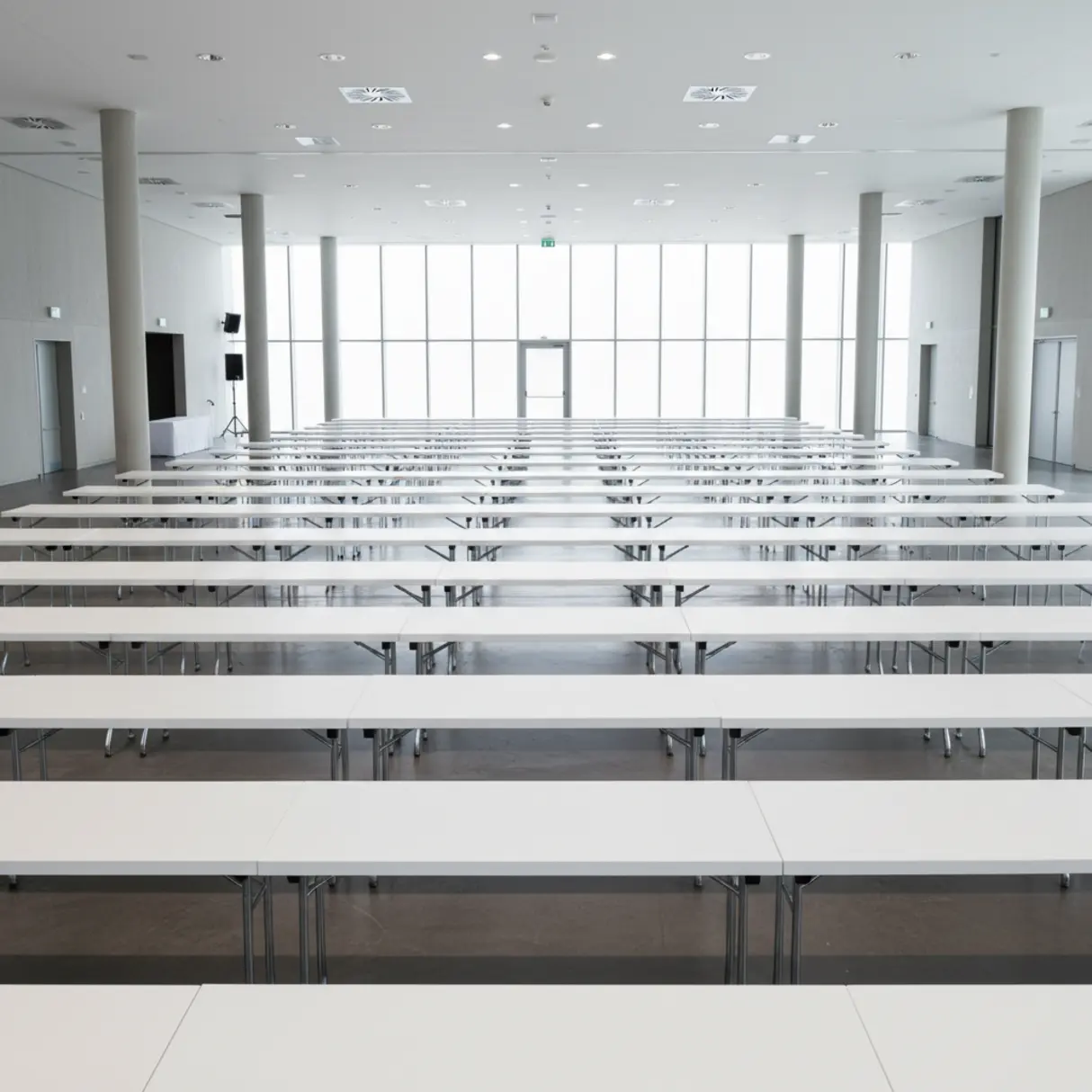 Białe stoły konferencyjne ustawione rzędami w jasnej, nowoczesnej sali.